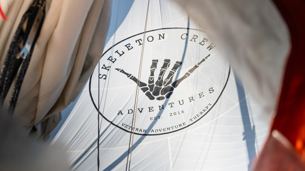 Skeleton Crew Adventures logo displayed on a white spinnaker sail, symbolizing offshore sailing and adventure therapy for veterans and first responders.